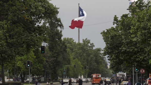 The Chilean flag flies as pedestrians cross a road in Santiago, Chile, on Saturday, Oct. 15, 2016. Chile's central bank will probably keep its benchmark rate at 3.5 percent for a 10th straight meeting as inflation slows to within policy makers' target range amid tepid economic growth. Photographer: Luis Enrique Ascui/Bloomberg