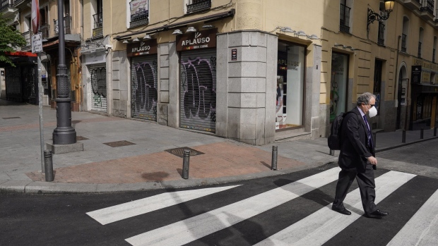 A commuter wearing a protective face mask uses a pedestrian crossing as shuttered stores line the street beyond in Madrid, Spain, on Thursday, May 7, 2020.