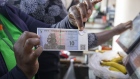 <p>A supermarket till operator displays a 10 ZiG banknote and 5 Zig coin in Harare.</p>