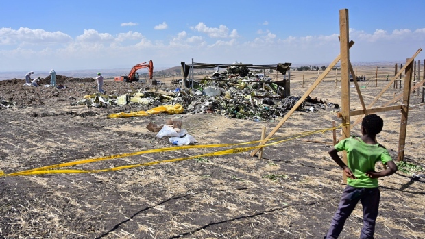 A boys look as forensic investigators comb the ground for DNA evidence near a pile of twisted airplane debris at the crash site of an Ethiopian airways operated Boeing 737 MAX aircraft on March 16, 2019 at Hama Quntushele village near Bishoftu in Oromia region.