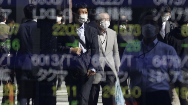 A pedestrian wearing a protective face mask is reflected in an electronic stock board outside a securities firm in Tokyo, Japan, on Thursday, Oct. 29, 2020. Japanese stocks pared losses after the Bank of Japan’s policy decision and as U.S. futures bounced back following a global equity rout. Photographer: Kiyoshi Ota/Bloomberg