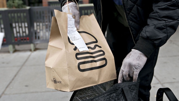 An Uber Eats delivery person places a Shake Shack take-out order into an insulated bag outside the restaurant in Washington, D.C., U.S., on Monday, April 20, 2020. Shake Shack Inc. will return a $10 million loan from the U.S. government amid criticism that the publicly traded burger chain and other larger companies gobbled up the emergency funding while smaller businesses were frozen out. Photographer: Andrew Harrer/Bloomberg