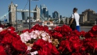 A pedestrian passes a flower bed in view of Tower Bridge and skyscrapers on the skyline of the City of London. Photographer: Simon Dawson/Bloomberg