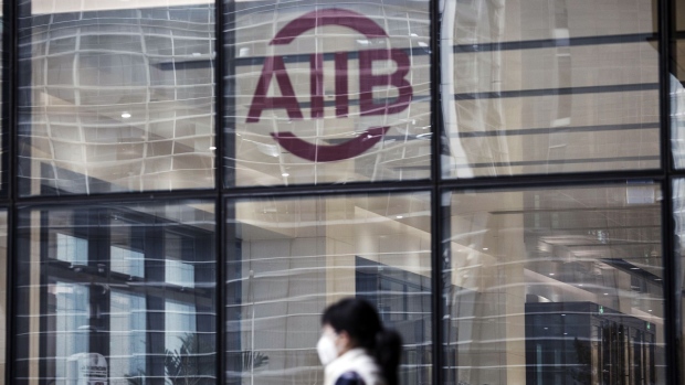 A woman wearing a face mask walks past a logo displayed at the Asian Infrastructure Investment Bank (AIIB) headquarters building in Beijing, China, on Thursday, Jan. 5 2017. One year after opening with 57 charter members, the China-led AIIB remains open to the U.S. joining, President Jin Liqun said. Photographer: Qilai Shen/Bloomberg