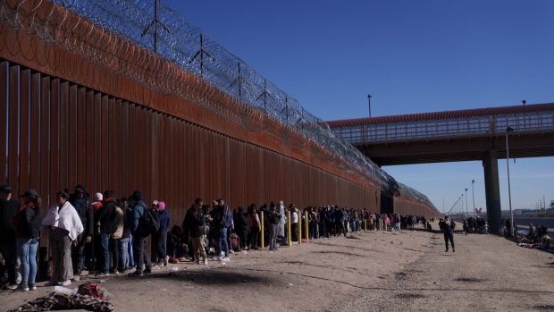 Migrants wait at the US and Mexico border wall in El Paso, Texas, US, on Thursday, Dec. 22, 2022. Chief Justice John Roberts temporarily blocked the scheduled ending of pandemic-era border restrictions while the US Supreme Court considers a bid by Republican state officials to keep the rules in place during a legal fight.