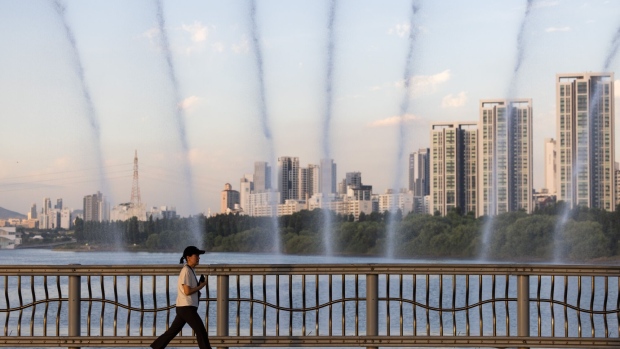 A pedestrain walks past water being sprayed from a fountain on Banpo Rainbow Bridge in Seoul, South Korea, on Thursday, Aug. 3, 2023. South Korea raised its heat wave warning to the highest level for the first time in four years earlier this week, with some parts of the nation experiencing temperatures above 38C (100.4F). Photographer: SeongJoon Cho/Bloomberg