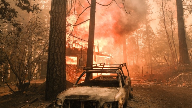 A structure burns behind a charred vehicle during a wildfire in Mariposa County, California, US, in 2022. Photographer: David Odisho/Bloomberg