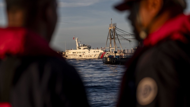 Philippine Coast Guard personnel looks at a Chinese Coast Guard ship and a Chinese fishing vessel, which Manila calls maritime militia vessel, during a resupply mission to the BRP Sierra Madre vessel in the disputed Second Thomas Shoal in the South China Sea, on Friday, Nov. 10, 2023. The latest mission to resupply Philippines' BRP Sierra Madre, a decaying World War II-era vessel on Second Thomas Shoal, was a display of the trilateral partnership between the Philippines, the US and Japan that is challenging Beijing’s efforts to control the disputed area. Photographer: Lisa Marie David/Bloomberg