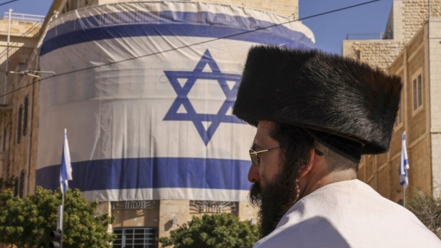 An ultra-Orthodox Jewish man walks past an Israeli flag. Photographer: Hazem Bader/AFP/Getty Images