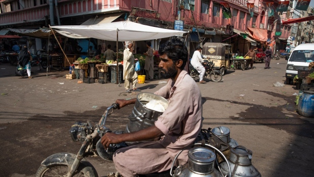 A motorcyclist transports milk churns through a market in Karachi.